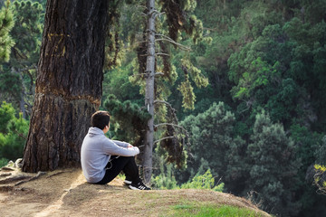 Fototapeta premium Hombre sentado en la cima de una montaña contemplando el bosque que lo rodea en calma 