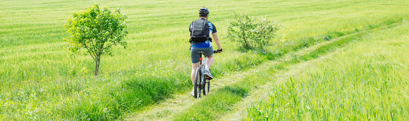man riding bicycle by trail in green barley field. copy space