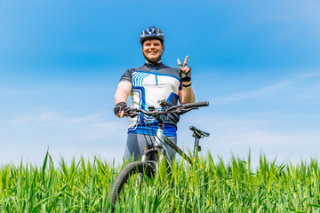 young adult smiling man standing with bicycle in green barley fi