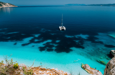 White catamaran yacht at anchor in calm clear azure water lagoon. Unrecognizable tourists relax and leisure on the hidden beach