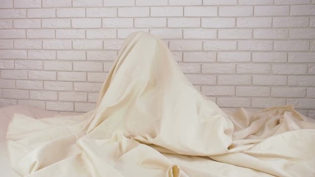 A child is playing in bed. The little girl is hiding under the blanket.