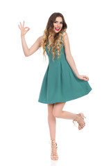 Beautiful Young Woman In Green Mini Dress And High Heels Is Showing Ok Hand Sign And Smiling
