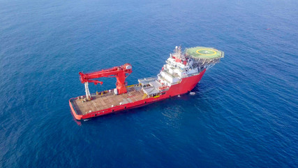 Aerial image of a Medium size red Offshore supply ship with a Helipad and a large crane