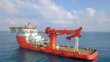 Aerial footage of a Medium size red Offshore supply ship with a Helipad and a large crane
