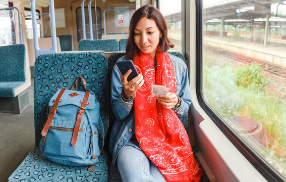 Young happy woman traveling by the train sitting near the window using smartphone