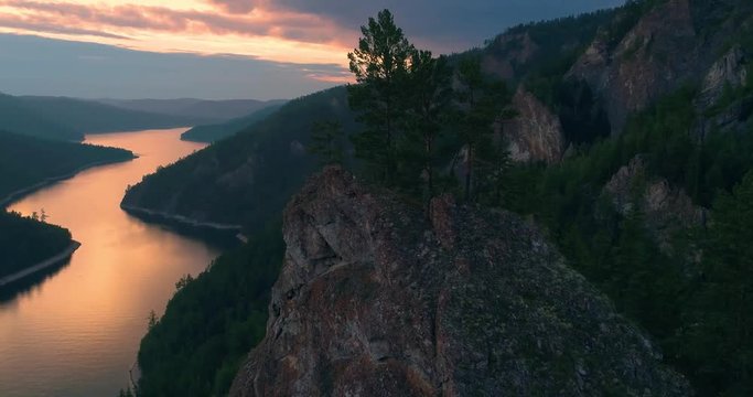 Beautiful rocks on the bank of the Yenisei river. Sunset reflected in the water of the river. Pine on a rocky cliff. Aerial View. Siberian taiga.