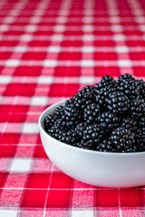 Vertical bowl of fresh picked blackberries, white ceramic bowl, red and white plaid tablecloth