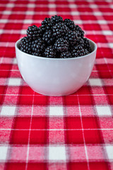 Vertical bowl of fresh picked blackberries, white ceramic bowl, red and white plaid tablecloth