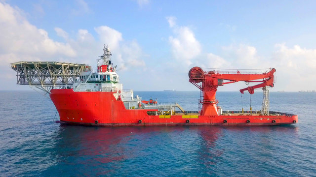 Aerial image of a Medium size red Offshore supply ship with a Helipad and a large crane