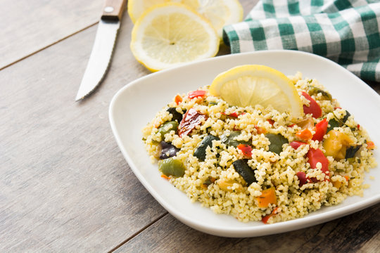 Couscous with vegetables in plate on wooden table
