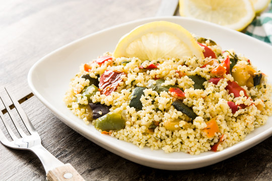 Couscous with vegetables in plate on wooden table