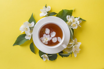 Cup of tea with petals of Jasmine flowers on a bright yellow background. Copy space,