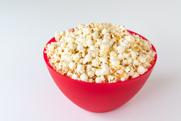 Popped popcorn in a big red plastic bowl on a white table