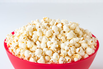 Close up of popped popcorn in a big red plastic bowl on a white table