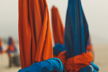 Beach umbrellas on foggy day in Deauville, fashionable holiday resort in Normandy, France. Folded colorful parasols in the morning on the empty beach. Leisure and seaside vacations concept. Close up