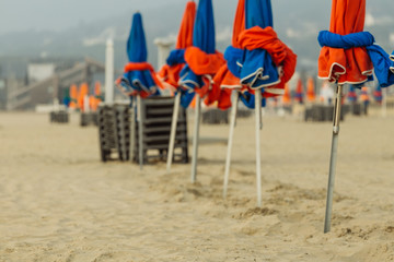 Beach umbrellas on foggy morning in Deauville, fashionable holiday resort in Normandy, France. Folded colorful parasols and lounge chairs on the empty beach. Leisure and seaside vacations concept.