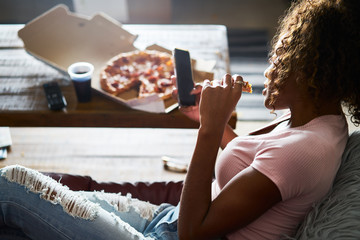woman laying on sofa watching tv and eating pizza late at night