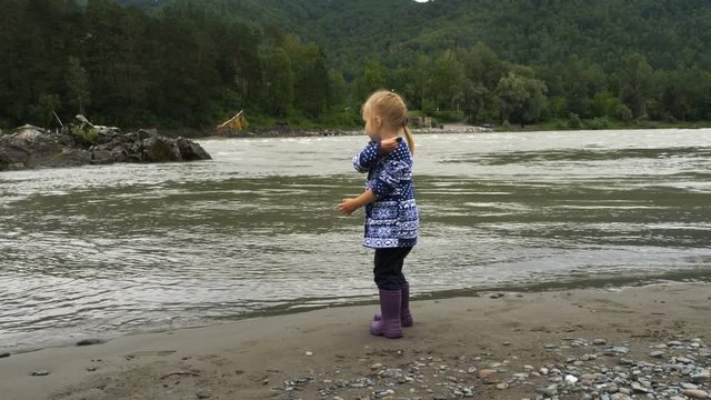 Blonde little girl throw stones in the river.