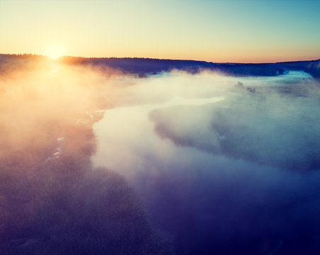 Early misty morning. Aerial view of countryside and river. The sun highlights the fog over the river