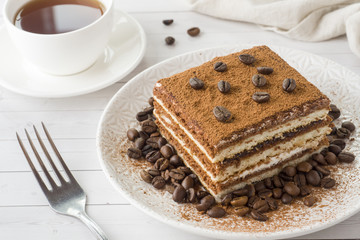 Delicious Tiramisu cake with coffee beans on a plate and a Cup of coffee on a light background