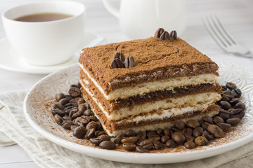 Delicious Tiramisu cake with coffee beans on a plate and a Cup of coffee on a light background