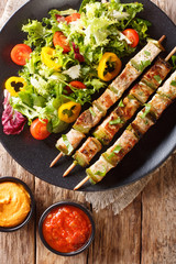 Pork shish kebab with vegetable fresh salad on a plate and sauces close-up. Vertical top view