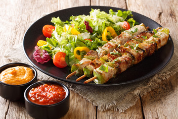 Freshly cooked kebabs with pepper on skewers with fresh salad on a black plate and ketchup and mustard close-up. horizontal