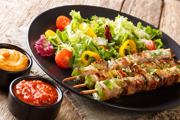 Barbecue pork with pepper on skewers with fresh salad on a black plate and ketchup and mustard close-up. horizontal