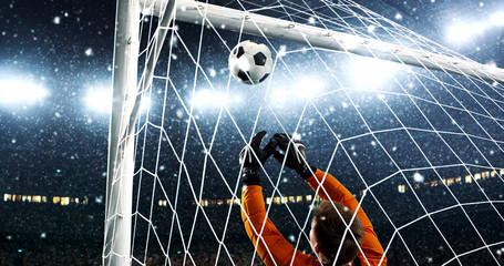 Goalkeeper tries to save from a goal on a professional soccer stadium while it's snowing.