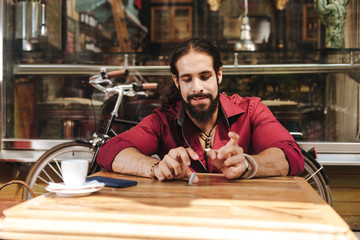 In the cafe. Delighted bearded man playing with a chip while sitting at the table in the cafe