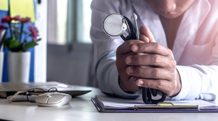 God and Health. Confident doctor praying with hands holding stethoscope.