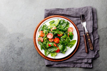 Fresh summer salad with baby spinach and tomatoes cherry. Top view, copy space. Slate gray background