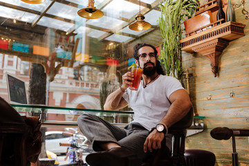 Fototapeta premium Tasty drink. Serious bearded man enjoying his cocktail while sitting in the cafe