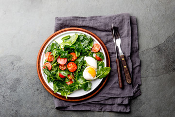 Fresh summer salad with baby spinach, tomatoes cherry and egg. Top view, copy space. Slate gray background