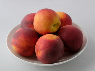 Still life of peaches. A few fresh peaches on a white plate.
