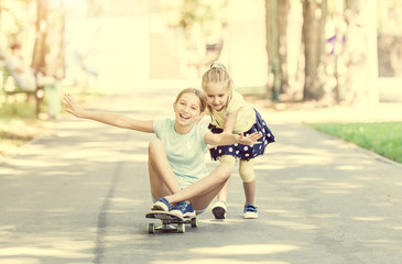 two little sisters playing with a skateboard