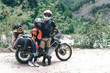 Obraz premium Happy young love couple in body armor and halmets stand with big adventure motorcycle, travel togather, jorney, copy spase, mountains dirt road, enduro road trip