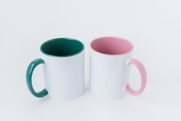 view from above Two white mugs, with a green and pink handle on a light background. Side view.