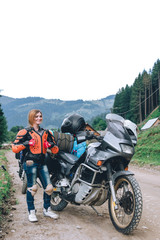 Fototapeta na wymiar happy girl in body armor like, stand alone a with big adventure touring motorcycle bags and camping equipment, off road travel jorney, traveling together, couple, mountains dirt road vertical photo