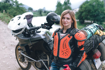 A girl dressed in body armor stand alone a with big adventure touring motorcycle with bags and camping equipment, off road travel jorney, traveling together, couple, mountains dirt road and river
