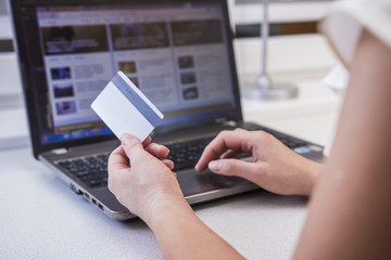 The girl is shopping on the Internet. In the hands of a plastic credit card. A woman in front of a computer monitor on the web page of an online store chooses clothes.