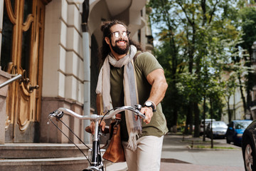 City style. Positive stylish man wearing sunglasses while riding in the city on a bicycle
