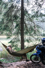 happy man relaxing lying in hammock on side mountain lake. Summer travel lifestyle. motorcycle off road adventure, vertical photo