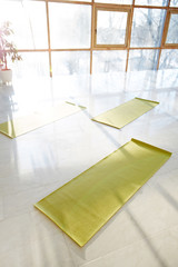 From above shot of arranged green yoga mats on white floor of light hall with sunlight shining through windows