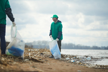 Two activists men working and collecting garbage to bags on polluted shore