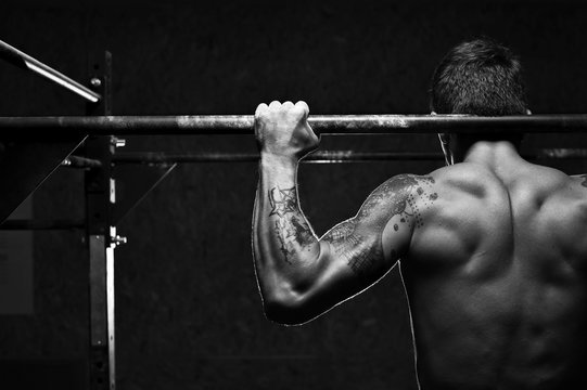 Close-up - muscular man doing pull up exercise on horizontal bar. Male athlete working out in the gym