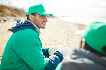 Two volunteers in green uniform sitting and having break on coast