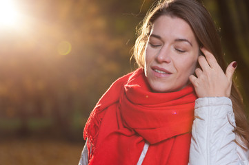 Happy autumn time. Positive beautiful woman wearing coat and red scarf on the background of nature park