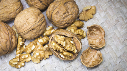 Assortment of walnut shells, walnut kernels and cracked walnut shells on light wicker surface.