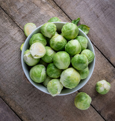Brussels sprouts in white bowl on natural wooden desk, top view.